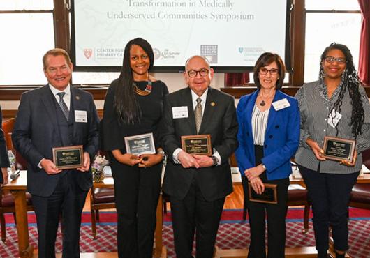 Seven panelists in a line, facing the camera, holding commemorative plaques