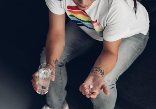  young transgender man with pill and glass of water sitting on couch 