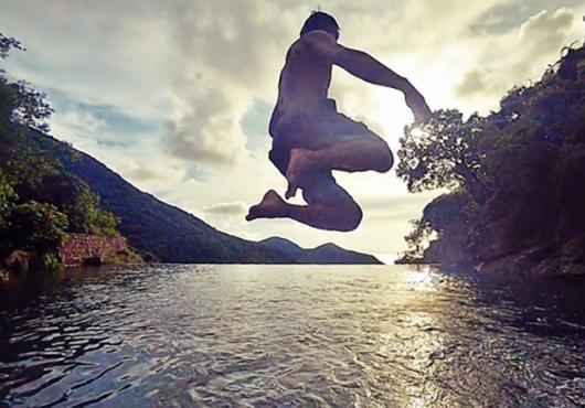 Will Chan jumping into a body of water, backlit