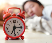 teen sleeping blurred in background with alarm clock in foreground
