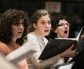 Photo of three chorus members singing during rehearsal