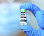 Photo of a hand wearing medical glove holding a vaccine vial