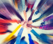 Many hands of different colored people reaching into center of a circle