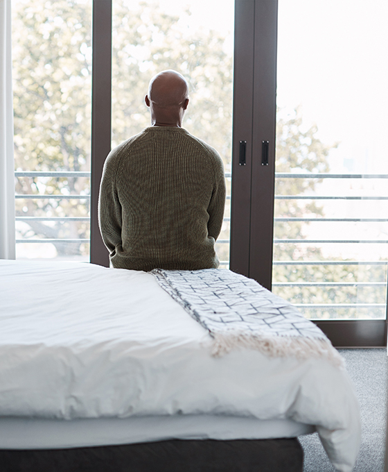 silhouette of a man alone sitting on bed looking out window