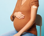 pregnant women with hand on her belly and other arm showing bandaid on arm after vaccination