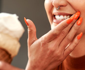 Cropped image of woman eating an ice cream cone and flinching and holding hand to mouth like in pain
