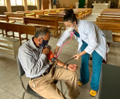 Sedas taking a patient's blood pressure in a church during the panemic; both are wearing masks