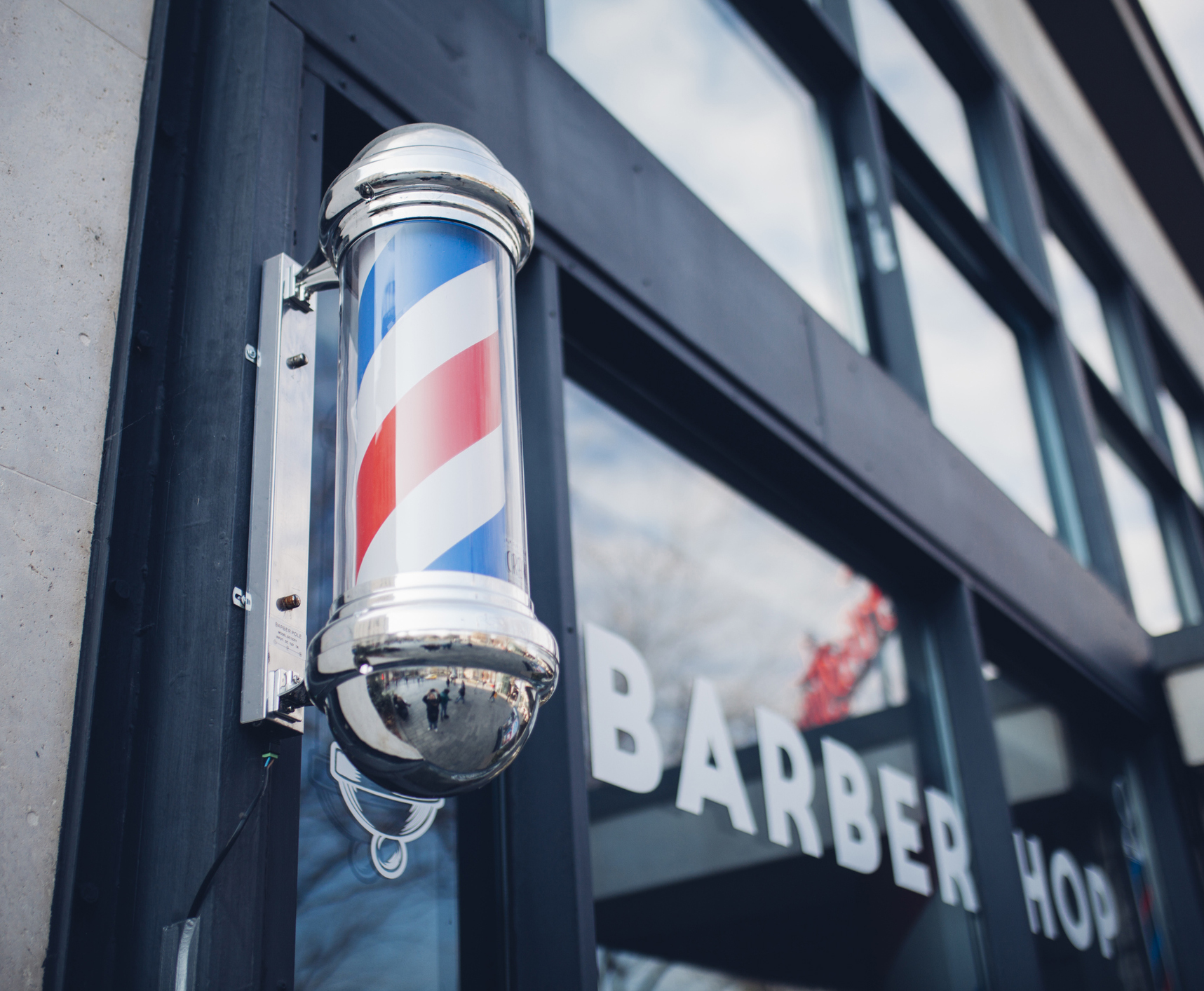Store front of a barbershop with a barber pole and white lettering on a glass door