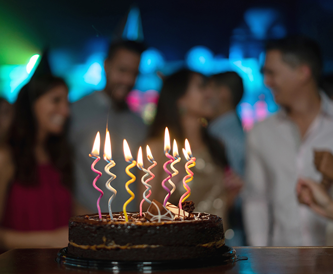 Birthday cake with lit candles and people blurred out in background