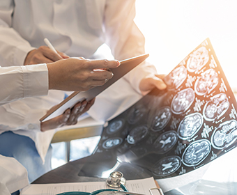 Closeup of the hands of two people wearing white lab coats examining medical images of a patient’s brain.