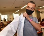 Male medical student wearing a mask putting on a white coat.