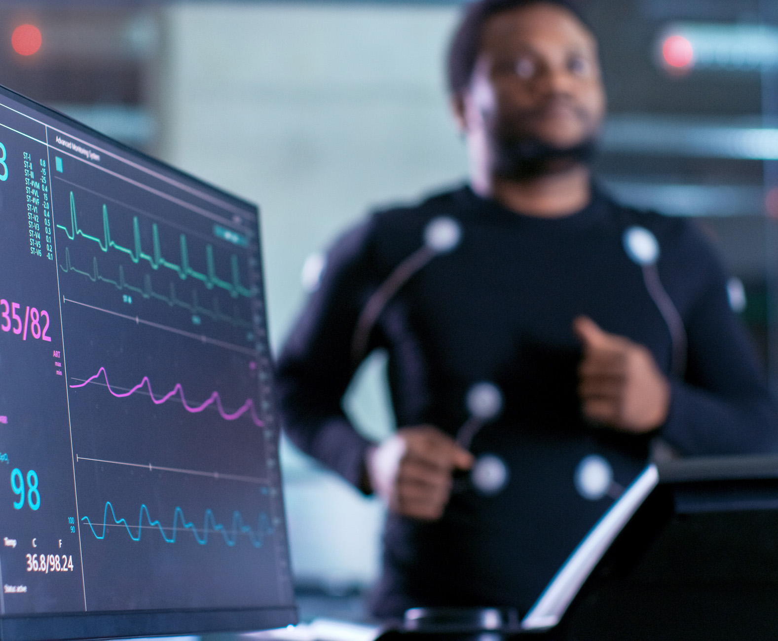 Blurred image of a man on a treadmill with electrodes attached and connected to a heart monitor in a research lab