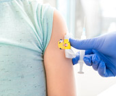 white child's arm with sleeve rolled up and a gloved hand holding a vaccine putting a bandage on the arm