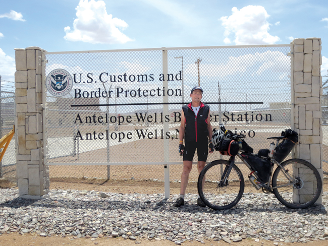 Nat Cobb with his bicycle next to a sign marking the community of Antelope Wells, New Mexico