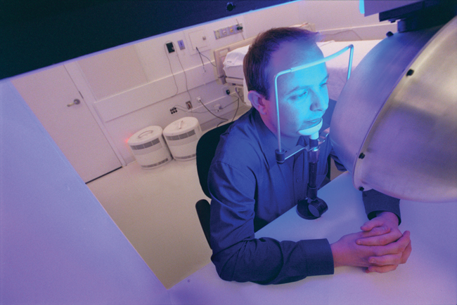 Steven Lockley seated in front of apparatus that is bathing his face in blue light