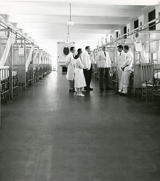 Image of mid-century photo, William Bosworth Castle, MD 1921 (center) talks with medical staff and faculty in a ward at Boston City Hospital
