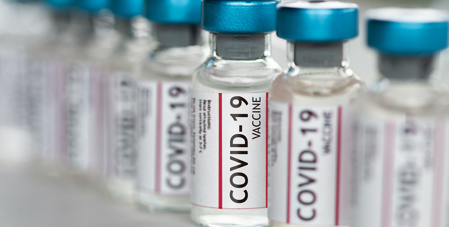 A row of vials labeled COVID-19 vaccine sits on a shelf.