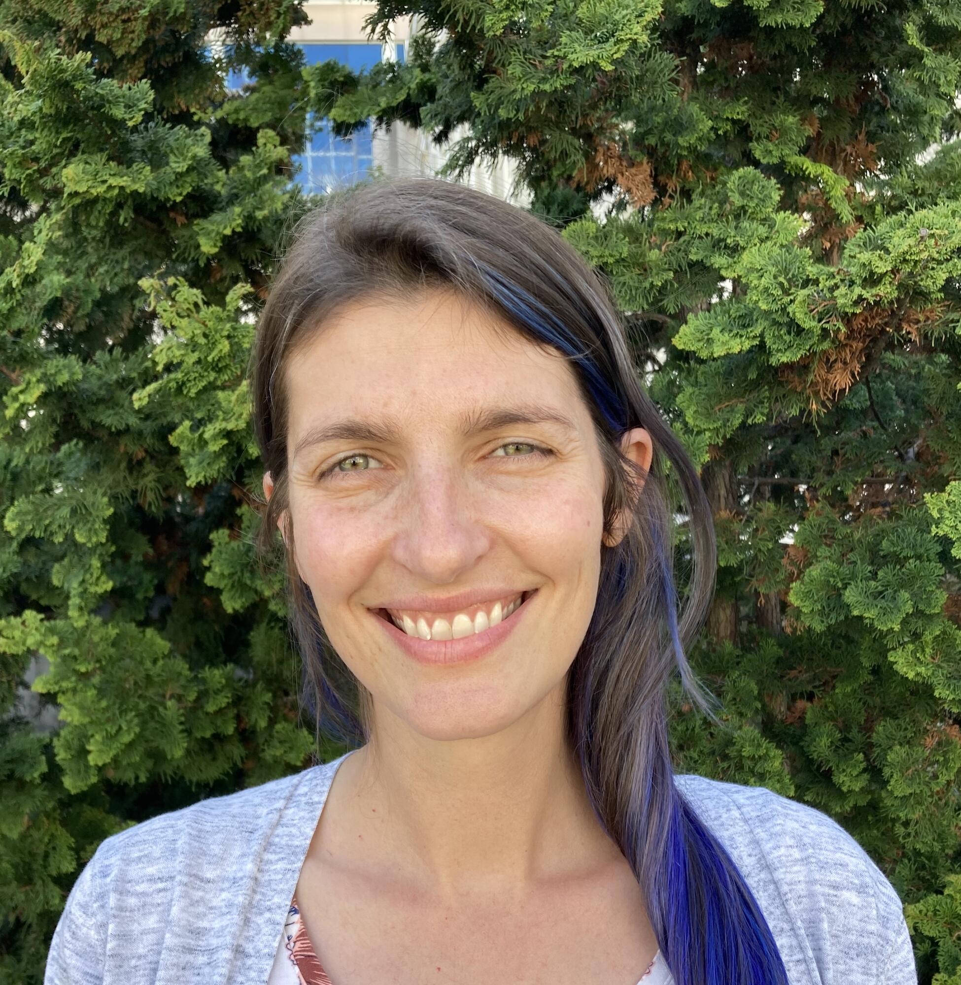 Head shot of a smiling woman with greenery in background