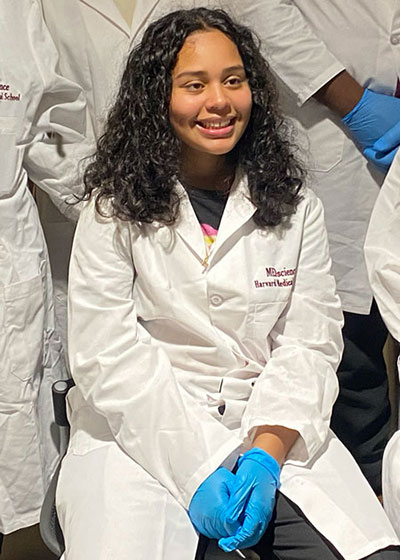 Jasmine Canas wearing white coat with MEDscience logo and blue latex gloves