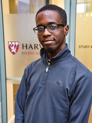 Student standing inside medical education building at HMS, in front of a glass door with HMS logo