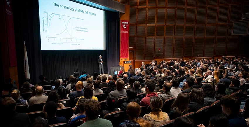 photo of a crowded auditorium. jennifer doudna stands in the distance below a large projector screen