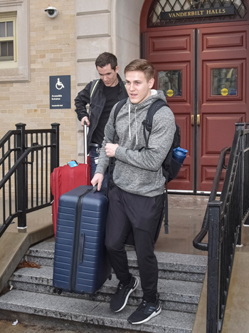 Two students carry suitcases down stairs outside main entrance to Vanderbilt Hall