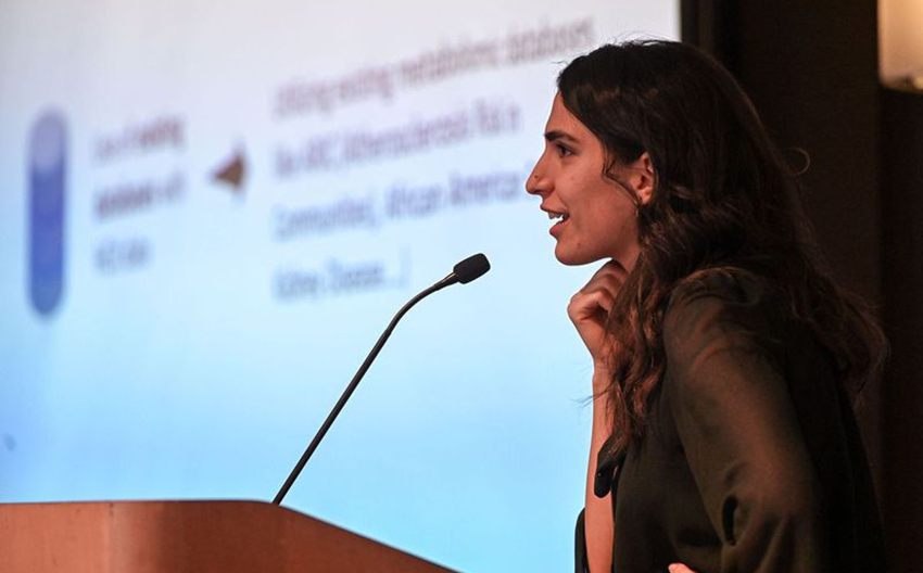 Side view of a young woman presenting at a lectern in front of a projected slide show