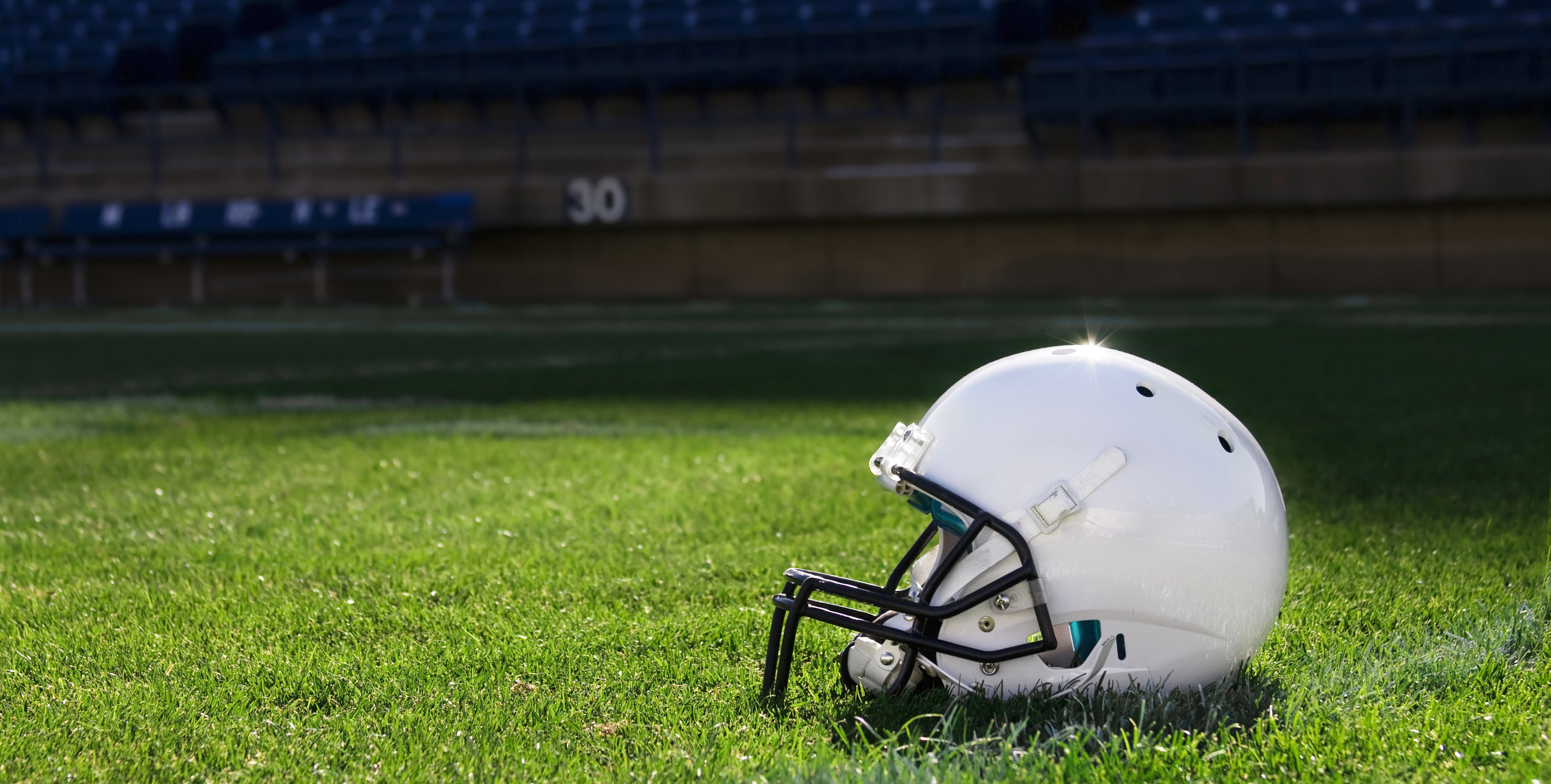 A white football helmet rests on a grass field in a stadium