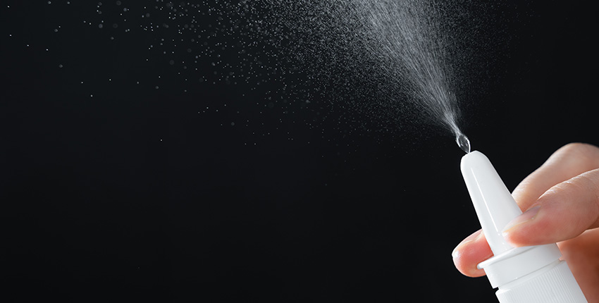 A closeup of a nasal spray nozzle releasing mist into the air