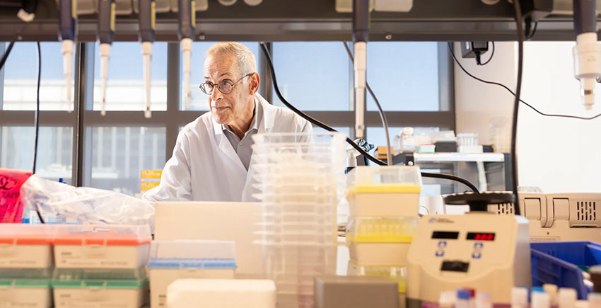 Photograph of a man in a white coat, with lab equipment in the foreground.