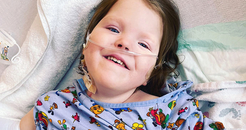 Photo of a young girl lying on blankets wearing a hospital gown featuring cartoon characters.