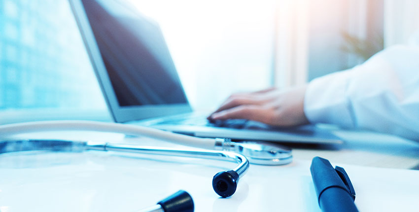 Close-up of a laptop, stethoscope, and physician’s forearm in white coat