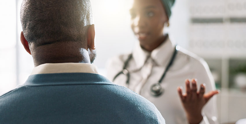 A photograph of a doctor (with face out of focus) talking with her patient, who has his back to the camera.