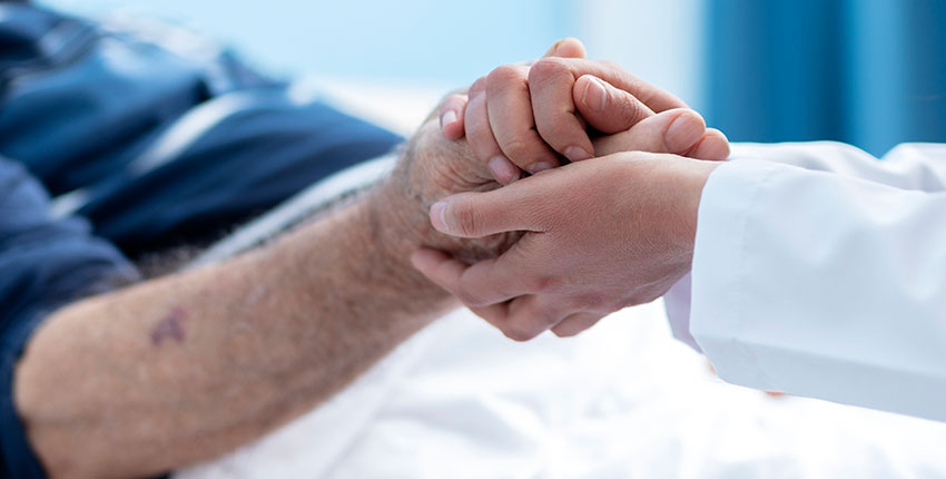 Close up of doctor in white coat holding the hand of an elderly patient