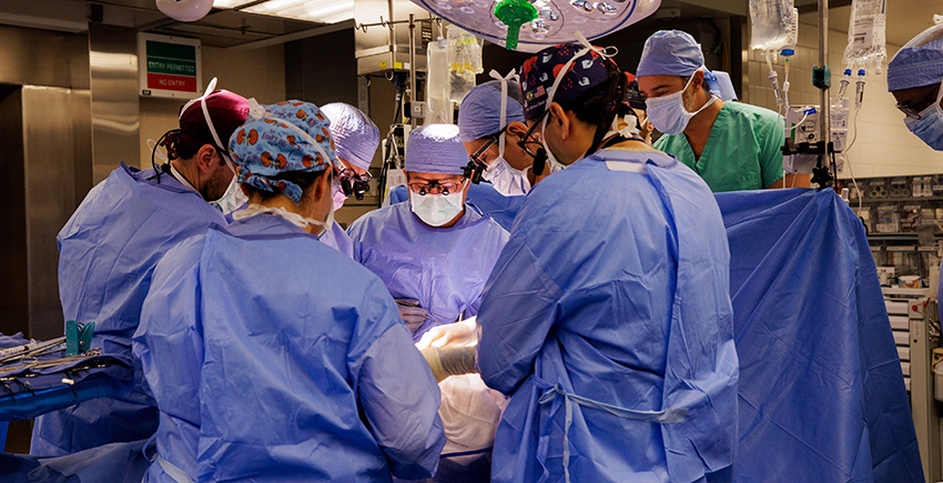 Eight people in surgical garb cluster around an operating table