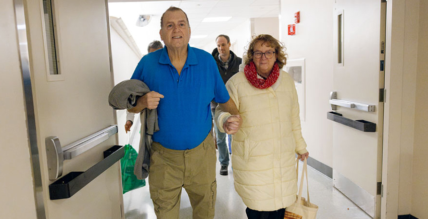 A man and a woman hold hands while walking down a hospital corridor.