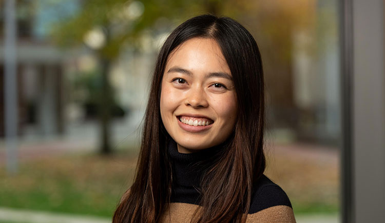 A woman on a blurred background smiles at the camera.