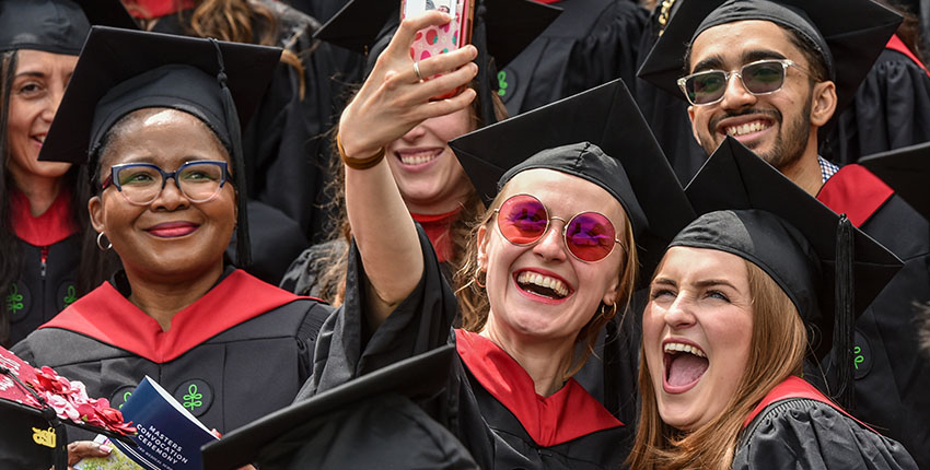 A woman holds up a cell phone to take a selfie with several other people.