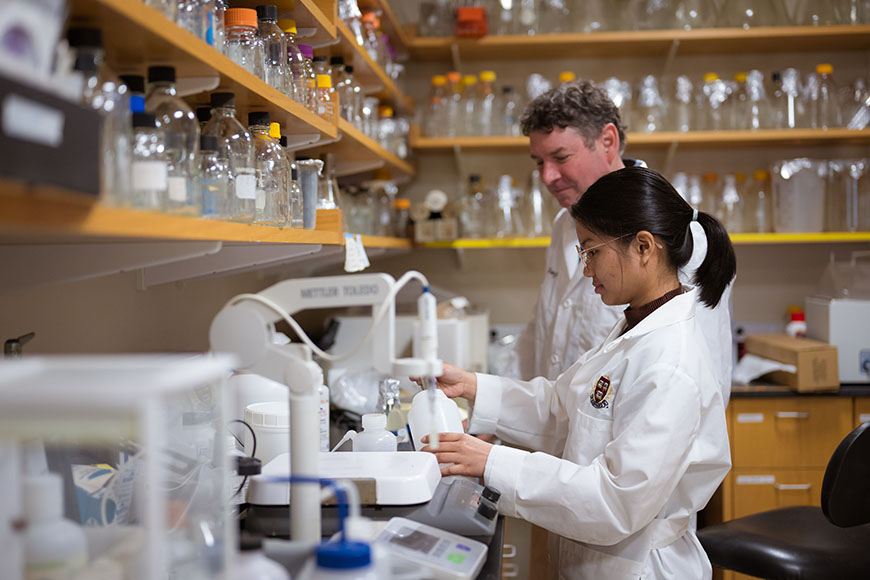 Two researchers work together in a microbiology lab at Harvard Medical School, surrounded by glass labware.