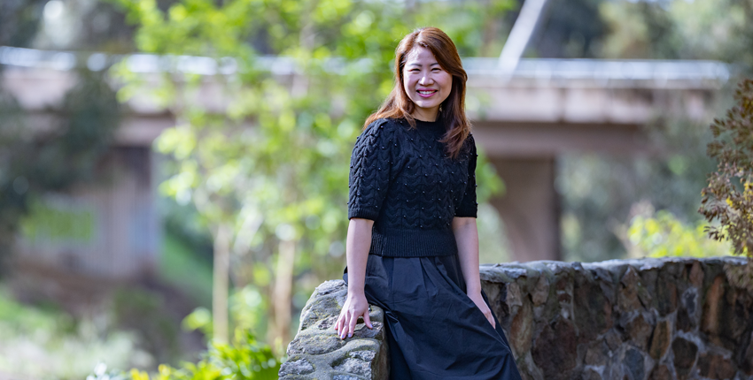 A woman sits on a stone wall and smiles at the camera