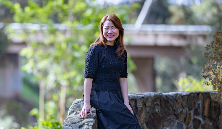 A woman sits on a stone wall and smiles at the camera