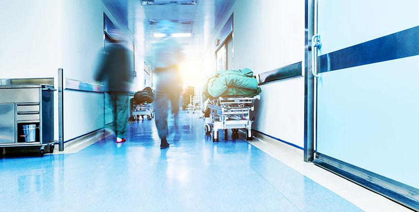 A backlit photo showing health care providers walking up a hallway away from the camera. The unsettling lighting and motion blur convey a sense of unease.