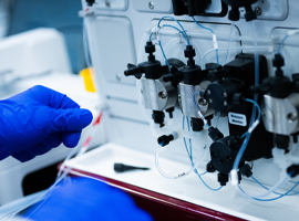 A gloved hand working with complex scientific lab equipment and tubes.