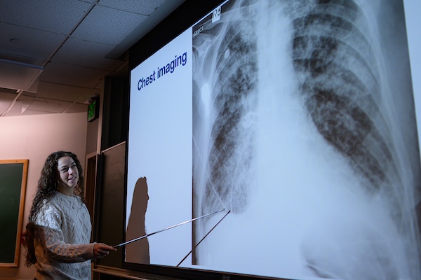 A student stands at a projected image of a chest imaging and points out their findings.