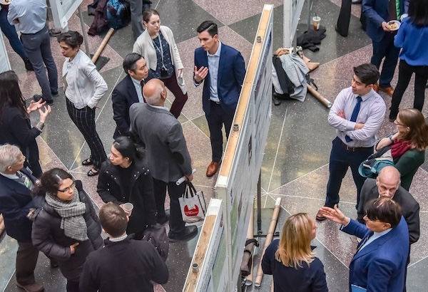 A scene from Soma Weiss Student Research day where students and faculty cluster in discussions about research posters mounted in rows in the Atrium.