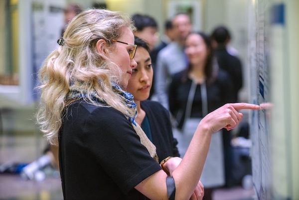 Two students converse while reading a research poster.