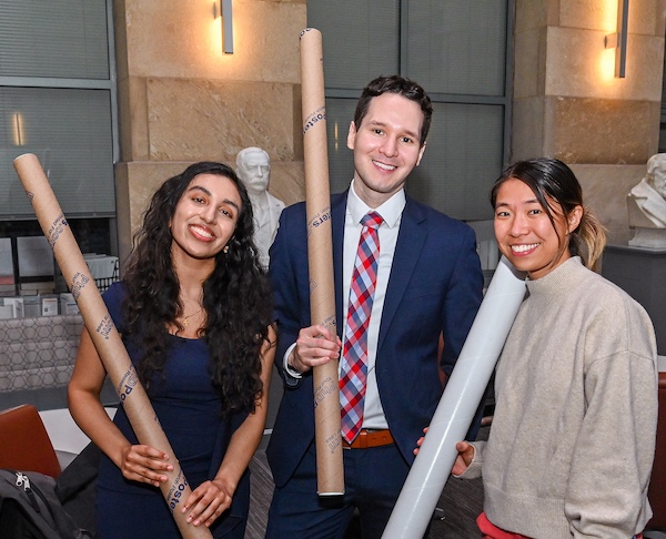 Three MD students pose together holding their research posters contained in a brown tube.