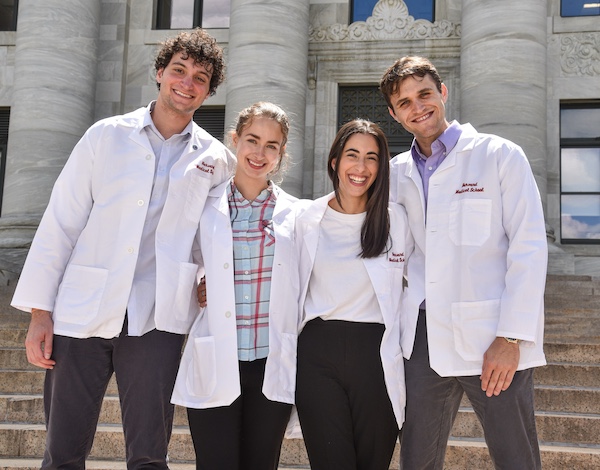Four MD students pose on the stairs in front of Gordon Hall.