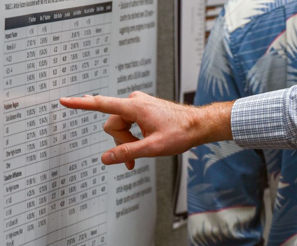 A close-up of a med student gesturing towards a scientific poster.