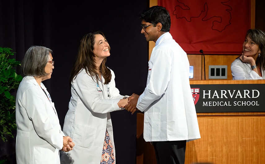 A student shakes hands with an advisor as other advisors smile on.